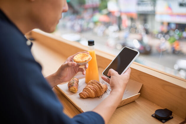 牛仔男性坐在带果汁和甜点的露台咖啡馆里 通过智能手机在互联网网站上搜索所需信息思考休闲帅哥