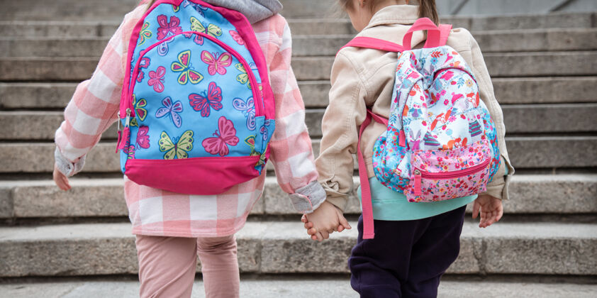 女生两个背着漂亮背包的小女孩手牵手一起上学童年友谊的概念友谊台阶孩子