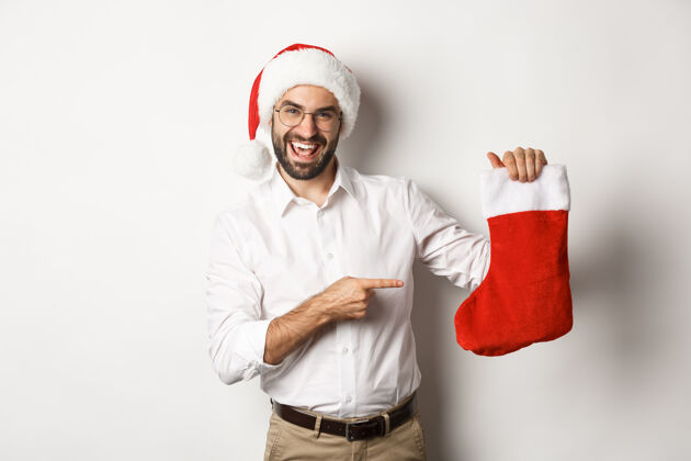 圣诞节圣诞老人戴着圣诞帽庆祝寒假 指着圣诞袜微笑着 拿着礼物 站着成人快乐商人