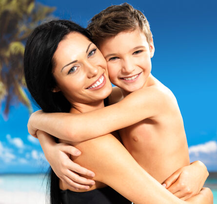 季节快乐微笑的母亲在热带海滩拥抱8岁的儿子的画像父母海岸自由