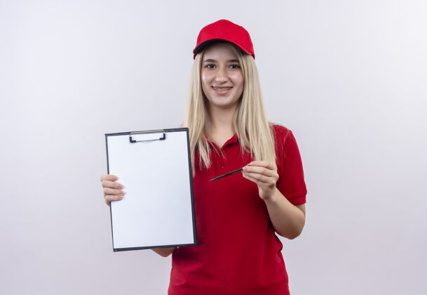 微笑微笑的小女孩穿着红色t恤 戴着帽子 戴着牙套 拿着剪贴板和铅笔 背景是白色的剪贴板持有铅笔