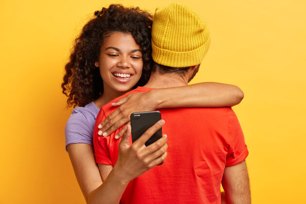 男朋友快乐微笑的美国黑人女子拥抱站在镜头前 拿着手机的男友浪漫电话拥抱