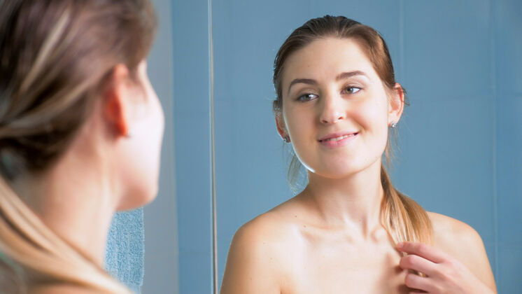 女士美丽的微笑的年轻女子 留着长发 看着浴室镜子里的自己涂抹毛巾脸
