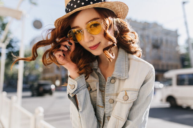 城市可爱的姜姑娘顽皮地摸着她的黄色太阳镜可爱的红发女子戴着帽子在城里消磨时光的户外照片女性快乐人