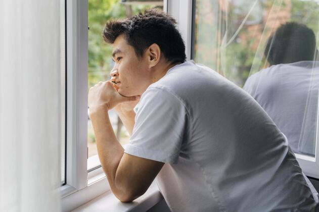 防护大流行期间 家里的男人透过窗户看外面隔离水平预防