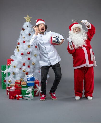 服装圣诞老人与男性厨师和圣诞礼物在灰色墙壁周围的正面视图庆祝厨师礼物