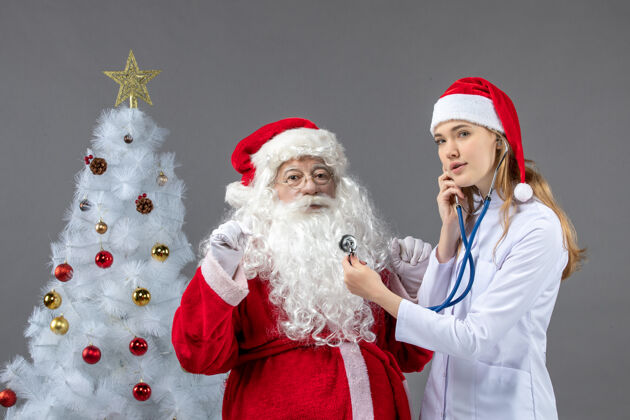 快乐圣诞老人的正面图 女医生拿着礼物站在灰色的墙上举行圣诞快乐女性