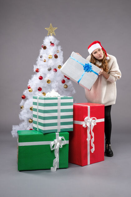 礼物年轻的女性在灰色的圣诞礼物周围圣诞树帽子玩具