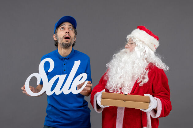 圣诞老人圣诞老人的正面图 男性信使手持销售横幅 灰色墙上挂着食品盒圣诞服装圣诞老人