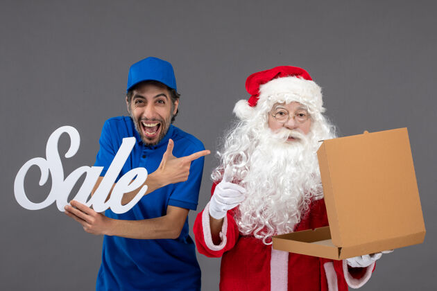 人圣诞老人的正面图 男信使拿着卖东西的字条 灰色墙上还有空的食品盒空信使十二月