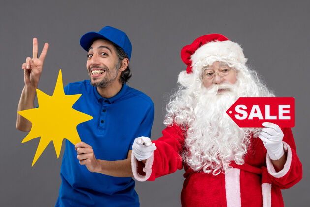 帽子圣诞老人的正面图 男性快递员手持销售横幅 灰色墙上有黄色标志男圣诞工作