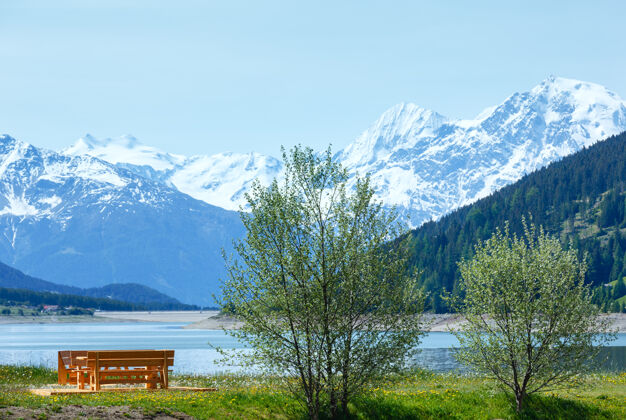 山Reschensee（或湖reschen）夏季景观与开花草地野餐木凳附近（意大利）雪山谷风景