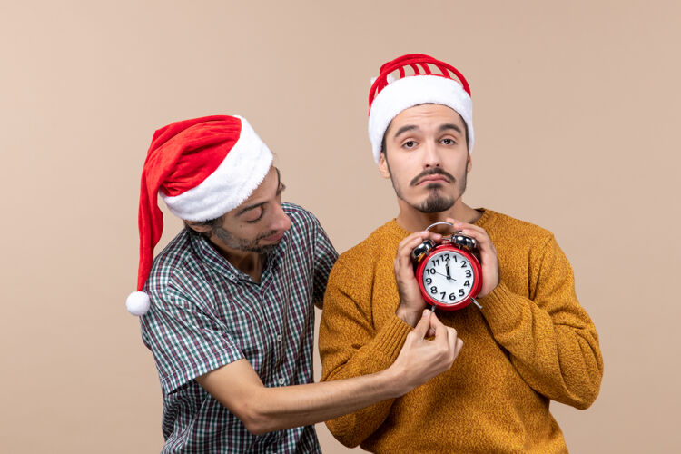 米色前视图两个圣诞老人一个双手拿着闹钟 另一个在米色背景上显示时间展示手前面