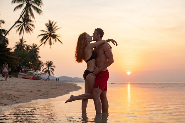 阳光年轻性感浪漫的情侣在夕阳下相爱 在夏日的沙滩上快乐地穿着泳衣一起玩关系男人女性