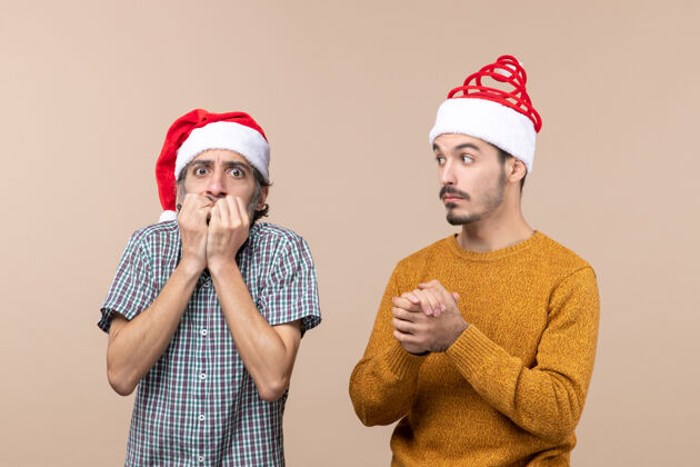男人前视图两个戴着圣诞帽的沮丧的家伙一个把手放在米色孤立背景上的鼠标上伙计们沮丧帽子