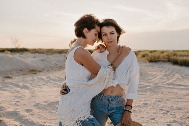 女同性恋两个年轻女子在日落海滩上玩得很开心 男女同性恋爱情浪漫拥抱女人开朗