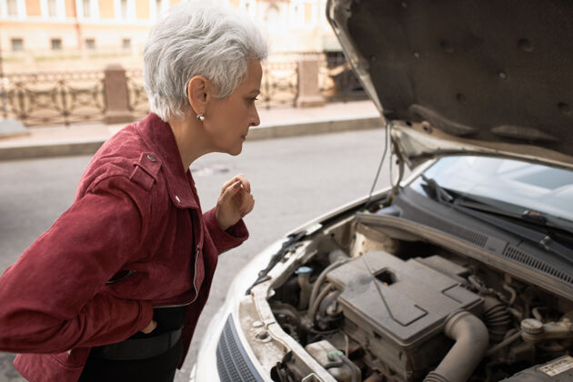 运输侧视图：沮丧的中年妇女站在开着引擎盖的车旁 往里看 试图找出问题所在车轮汽车麻烦