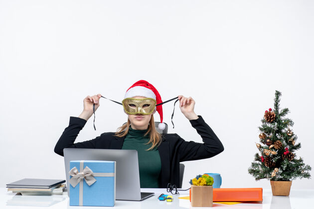 电脑圣诞节的心情与年轻女子戴着圣诞老人的帽子 戴着面具坐在一张桌子上的白色背景镜头桌子企业家圣诞老人