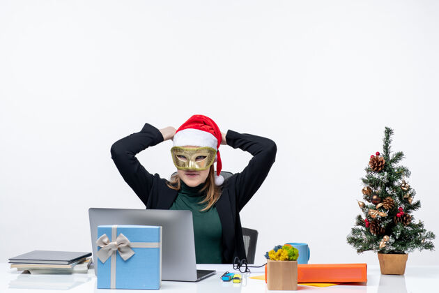 年轻女人圣诞气氛与戴着圣诞老人帽子和面具的年轻女子坐在白色背景的桌子旁工作面具桌子