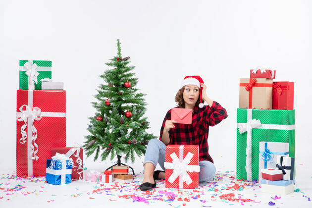 装饰前视图年轻女子坐在周围的礼物举行信封上的白墙圣诞快乐快乐人