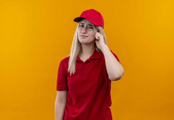 帽子悲伤的交付年轻女孩穿着红色t恤和帽子把她的手指放在孤立的橙色背景的头上红色年轻女孩