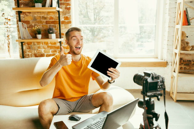 视频博客年轻的白人男性博主 带着专业相机 在家里录制平板电脑的视频评论博客 视频博客 视频博客关于照片或技术新颖性的男人制作视频博客或直播流成人微笑评论人