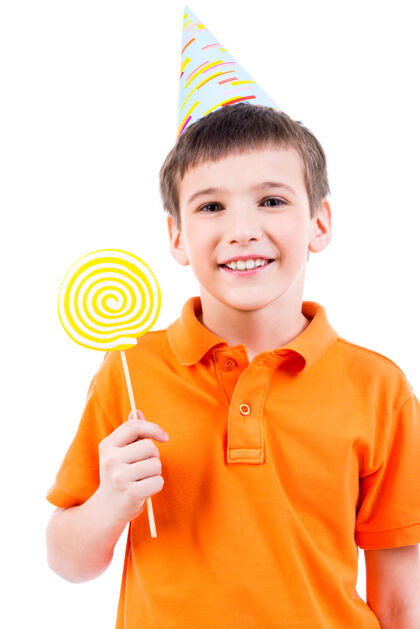 衬衫微笑的男孩穿着橙色t恤 戴着彩色糖果的派对帽-白色隔离糖果甜食食物
