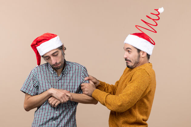 帽子正面图：两个戴着圣诞帽的家伙 一个困倦的 一个好奇的 抱着其他人的胳膊 背景是米色的帽子前面男人