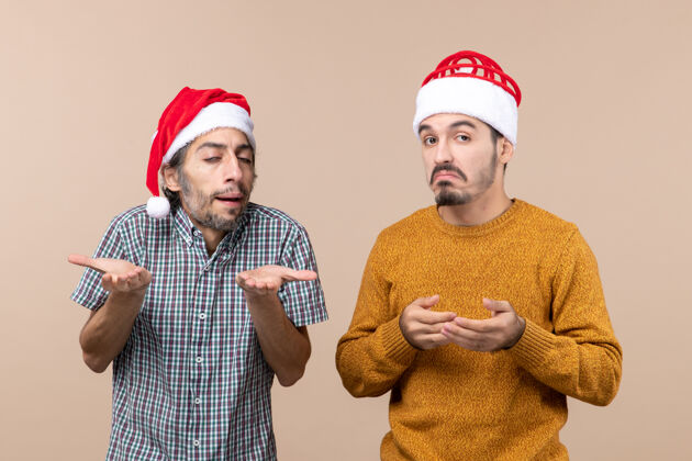 风景前视图两个戴着圣诞帽的家伙在米色孤立的背景下迷惑伙计们米色前面
