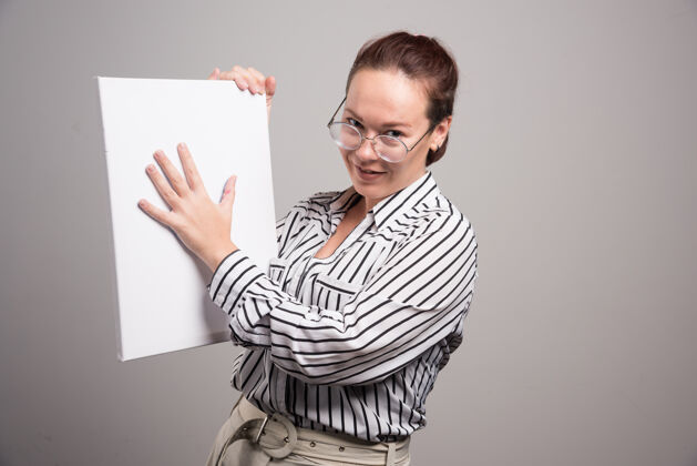 手一个女人在灰色背景上展示她的白色画布年轻人印刷