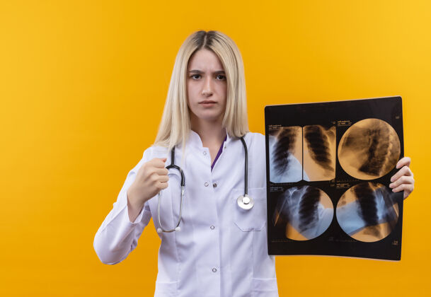 黄色严格的医生年轻女孩穿着医用长袍 手持听诊器 在孤立的黄色背景上拍x光片长袍医生穿着