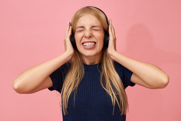 耳机有趣的情绪化的欧洲年轻女性戴着牙齿支架戴着无线耳机闭上眼睛 手放在耳朵上的孤立肖像播放器年轻乐趣