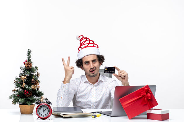 微笑圣诞节心情与年轻的胡须惊讶的商人与圣诞老人帽子举行银行卡和显示两个白色背景男性人成人