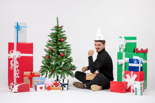 礼物年轻人坐在白色墙上的节日礼物周围的正面视图圣诞快乐人快乐