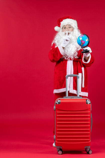 圣诞快乐圣诞老人的前视图 包里装着小地球仪 准备在红墙上旅行节日圣诞老人人