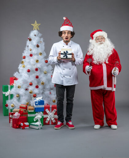 节日圣诞老人与男性厨师和圣诞礼物在灰色墙壁周围的正面视图服装正面厨师