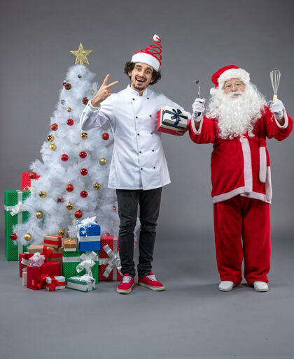 节日圣诞老人与男性厨师和圣诞礼物在灰色墙上的正面视图圣诞礼物圣诞老人