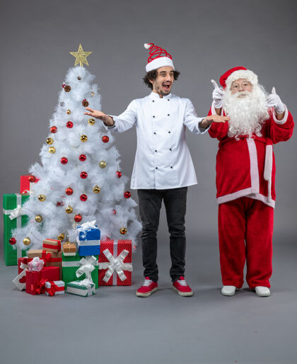 快乐圣诞老人和男厨师在灰色墙上围着圣诞礼物的正视图礼物圣诞老人圣诞老人