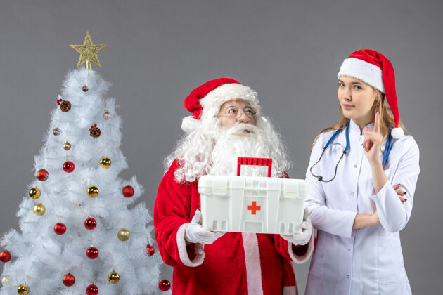 援助圣诞老人和给他急救箱的女医生在灰色墙上的正视图第一十二月圣诞老人
