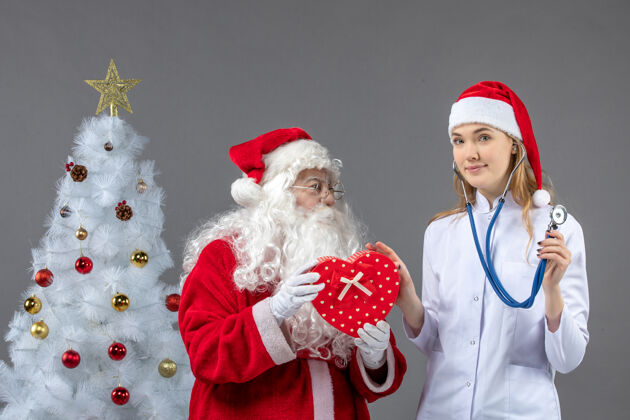 男性圣诞老人和女医生的前视图 女医生在灰色墙上用听诊器观察礼物圣诞快乐观察女性