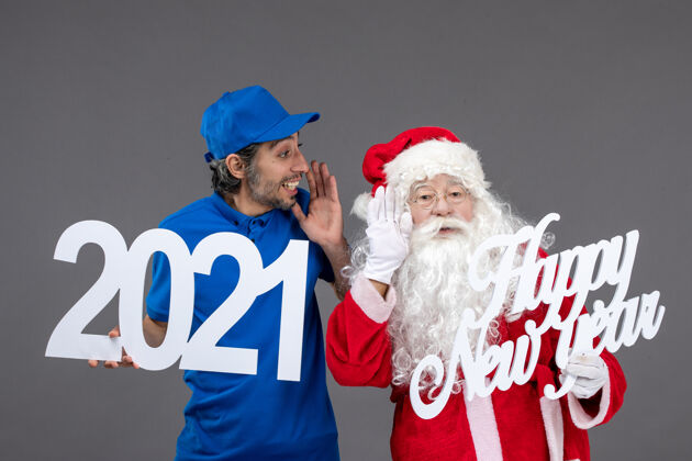 男人圣诞老人与男信使举行和新年快乐和2021年板灰墙的正面视图人们快乐圣诞