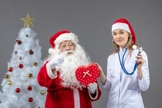 圣诞老人圣诞老人的正面图 女医生拿着礼物站在灰色的墙上十二月微笑男人