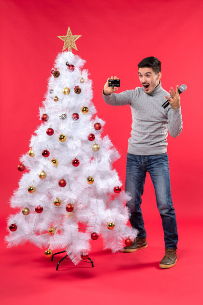 男孩圣诞节心情与情绪化的家伙站在装饰圣诞树附近 手持麦克风和电话情绪化微笑季节