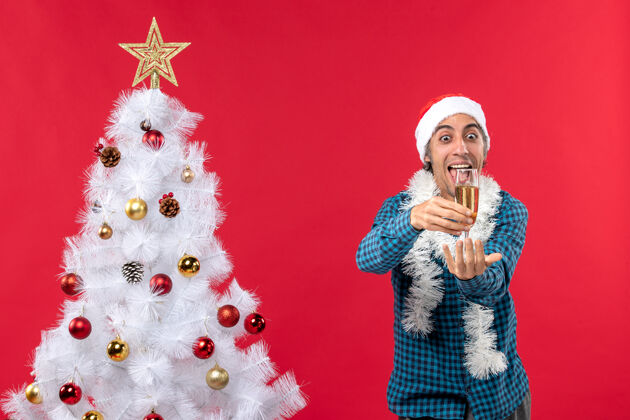 礼物圣诞节心情与情绪有趣的年轻人与圣诞老人帽子在一个蓝色条纹衬衫举起一杯葡萄酒附近圣诞树帽子养育夏娃