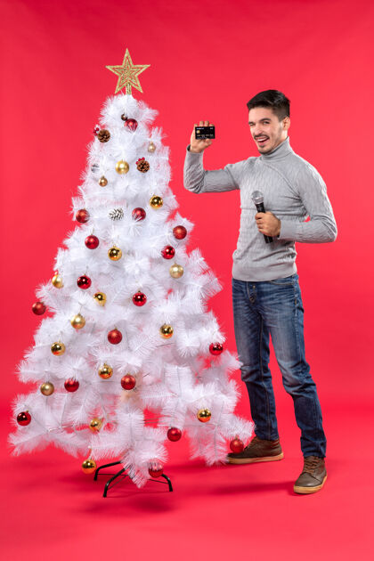 装饰圣诞气氛 微笑的年轻人站在装饰好的圣诞树旁 拿着麦克风和电话心情抱着微笑