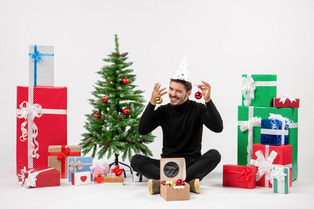 圣诞树正面图：年轻人围坐在白色的墙上 手里拿着圣诞礼物前面人坐着