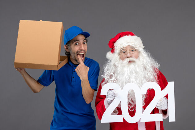 人圣诞老人的正面图 男信使手持2021横幅和灰墙上的食品盒肖像圣诞老人十二月