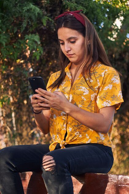 长凳一个年轻女孩坐在长凳上看手机的镜头衬衫树手机