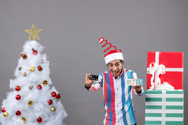 旅行前视图兴高采烈的年轻人拿着卡片和旅行票围着圣诞树和礼物年轻抱着礼物