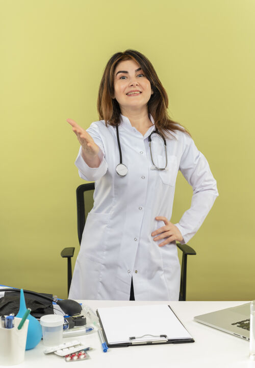 医生微笑的中年女医生穿着医用长袍 手持听诊器 站在办公桌后面 拿着医用工具 手持相机 还有复印空间办公桌手持女